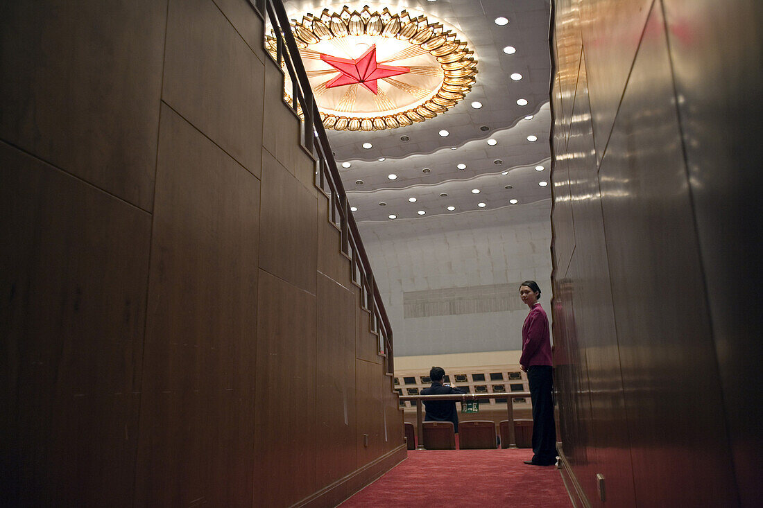 A Chinese attendant in the Great Hall of the People, near a ceiling decoration of a giant red star, during a session of the National People's Congress, China's Parliament.