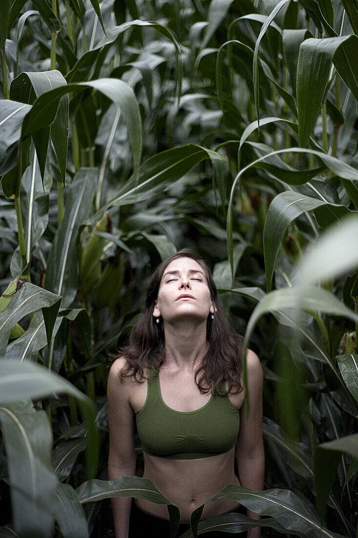 A beautiful young woman stretches towards the sky in the middle of a New Hampshire corn field.
