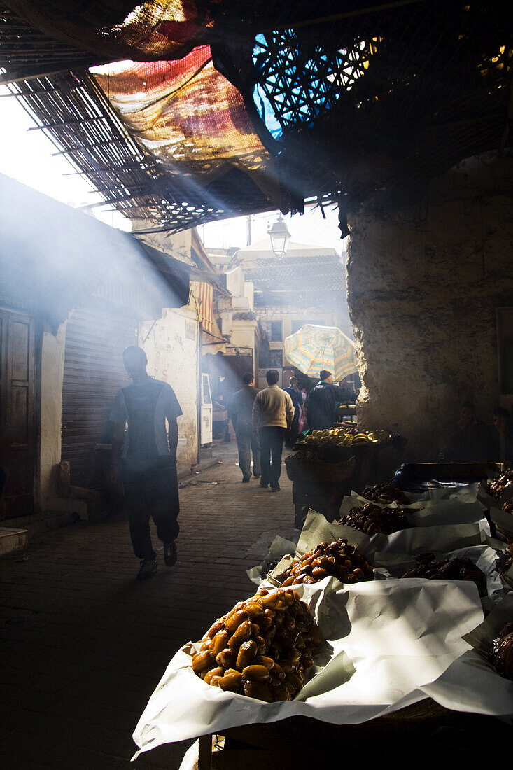 A shaft of light illuminates piles of large dried dates on sale at a street stall in a dark, busy street in Fes El-Bali, Morocco, on October 31, 2007.