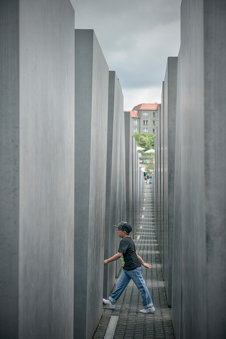 Young boy walking in between columns of the Holocaust Memorial, memorial for the murdered Jews of Europe, Berlin, Germany