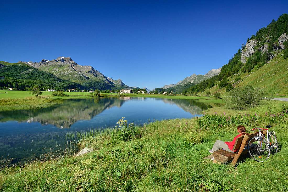 Radfahrerin rastet auf einer Bank mit Blick über den Inn auf Sils-Baselgia, Sils, Oberengadin, Engadin, Graubünden, Schweiz