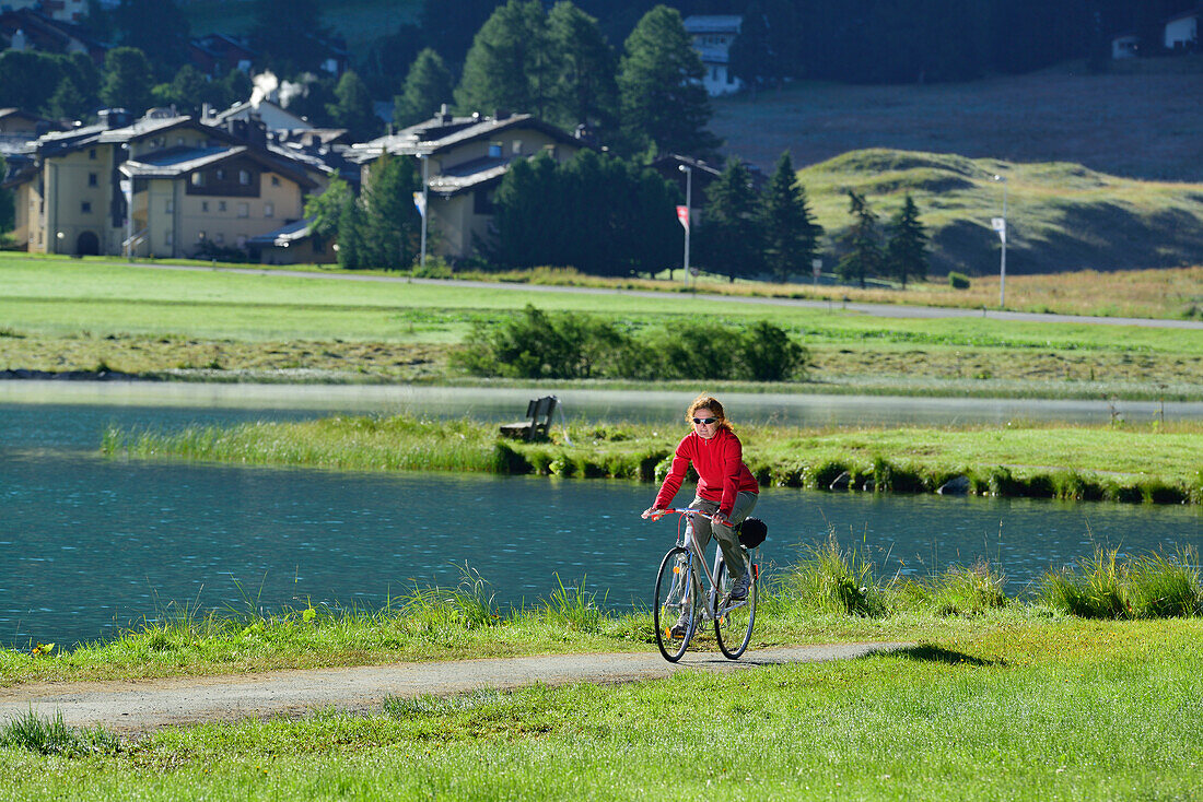 Woman cycling along Lake Champfer, Silvaplana, Upper Engadin, Canton of Graubuenden, Switzerland