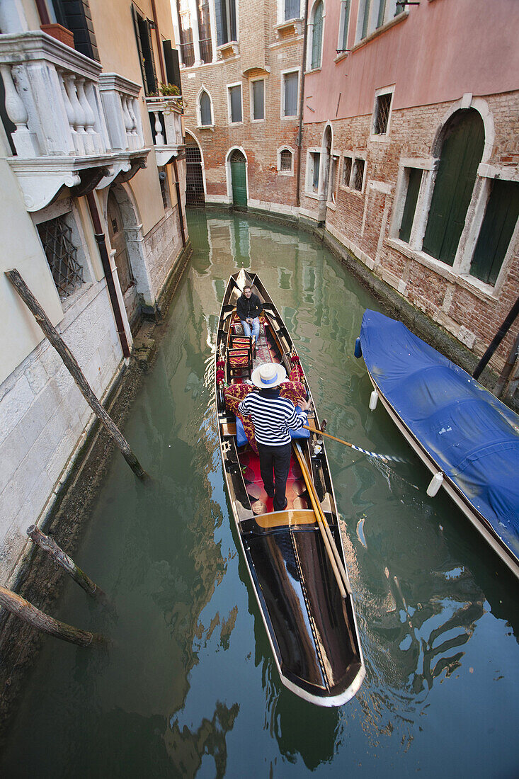A gondola with tourists sails through a narrow canal in Venice, Italy.