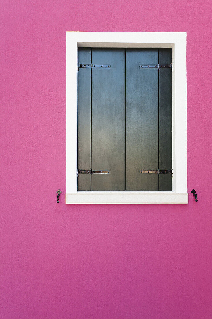A black window is framed on a colorful pink wall at Burano, Italy.