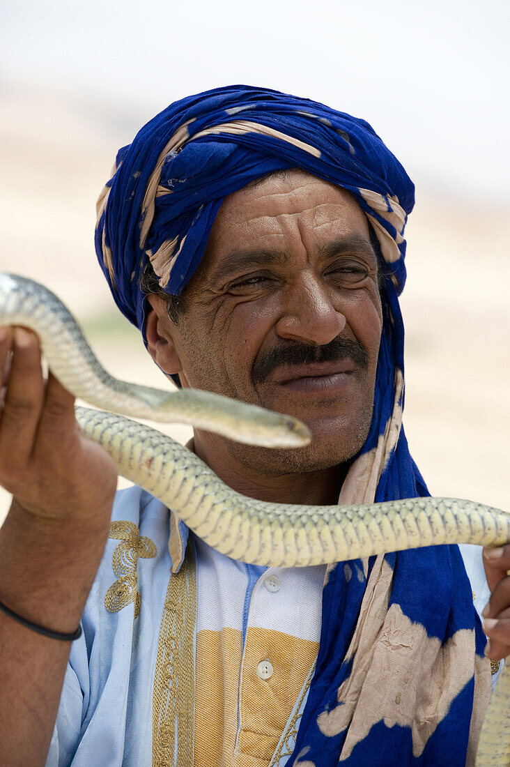 A local snake charmer lures the tourists to the roadside stand by handling a venomous snake in Morocco.