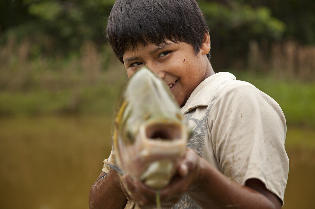 Young boy posses for a photo with a fish on a fish farm near Puerto Maldonado, Peru, March 3, 2011.