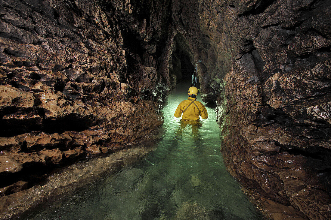 A very cold and wet British male cave explorer stands waist deep in the narrow stream passage leading to the sump pool of the classic famous cave in France called The Gouffre Berger high in the Vercors region.