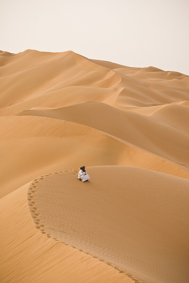 A man sits alone on the sand dunes of the Empty Quarter, Ar Rub Al Khali, Oman.