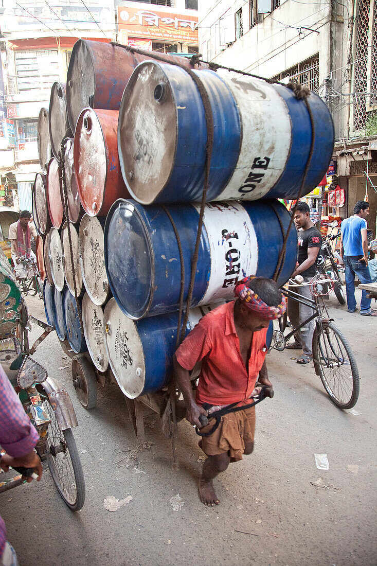 Dhaka,  Bangladesh - July 2011: Busy street  in Dhaka,  Bangladesh with a man pulling a wagon loaded high with 20 oil drums.