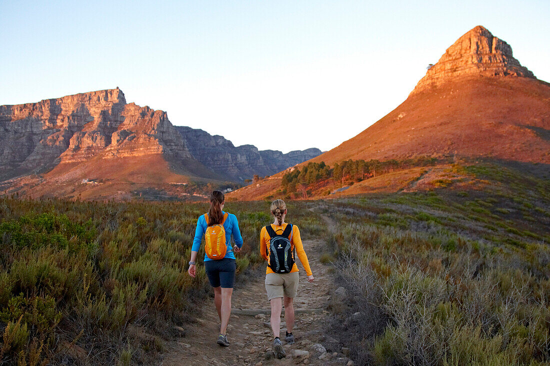 Katrin Schneider and Susann Scheller walking on the trail between Signal Hill and Lion's Head above the city of Cape Town just after sunrise. Cape Town, South Africa.