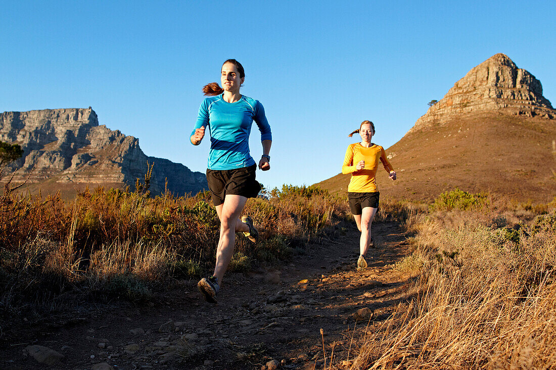 Katrin Schneider and Susann Scheller running on the trail from Lion's Head to Signal Hill above the city of Cape Town just after sunrise. Cape Town, South Africa.