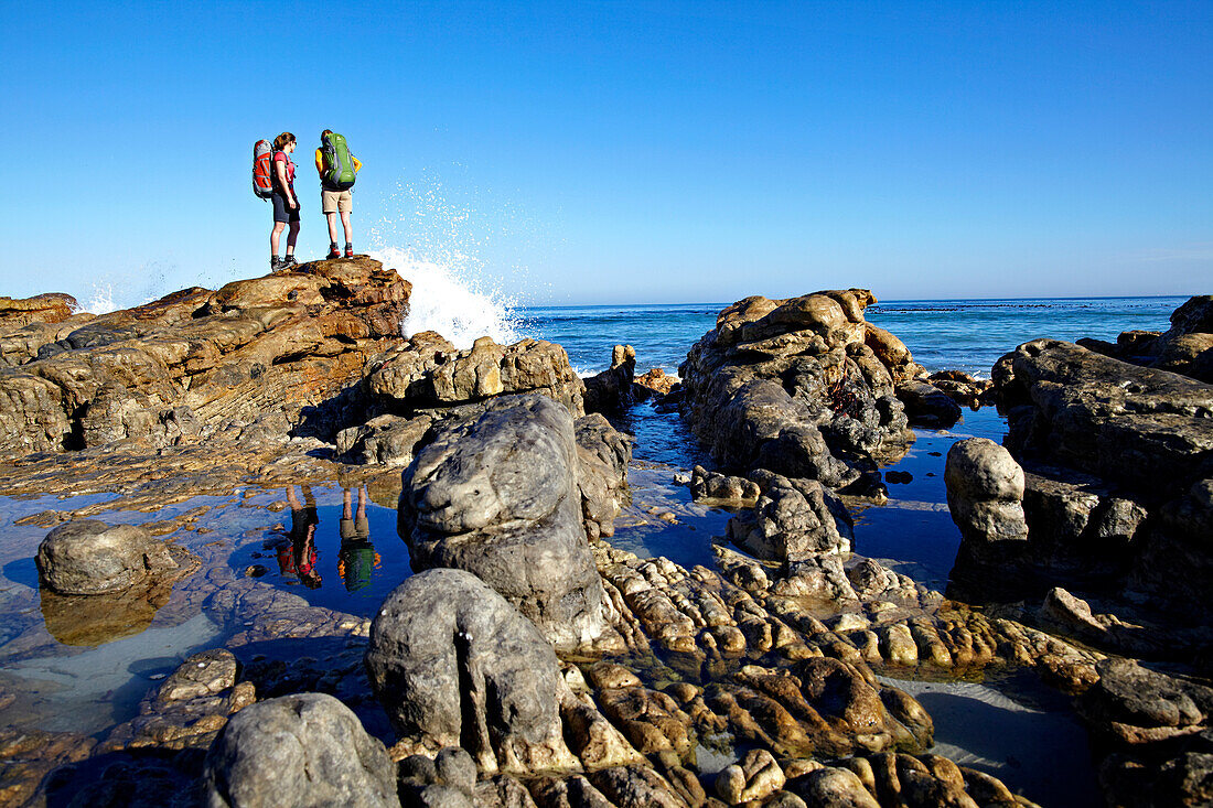 Katrin Schneider and Susann Scheller hiking along a rocky part of Noordhoek Beach along the Hoerikwaggo Trail which leads from Cape Point to Table Mountain in Cape Town. South Africa.