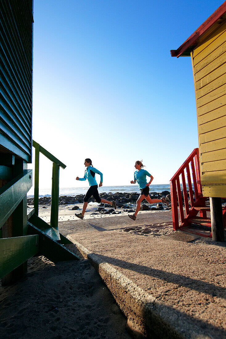 Katrin Schneider and Susann Scheller running past the famous and colorful bathing huts in St.James near Muizenberg. Cape Town, South Africa.