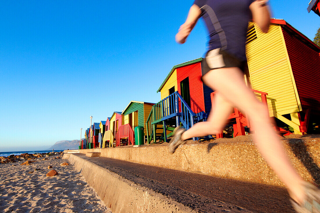 Katrin Schneider running past the famous and colorful bathing huts in St.James near Muizenberg. Cape Town, South Africa.
