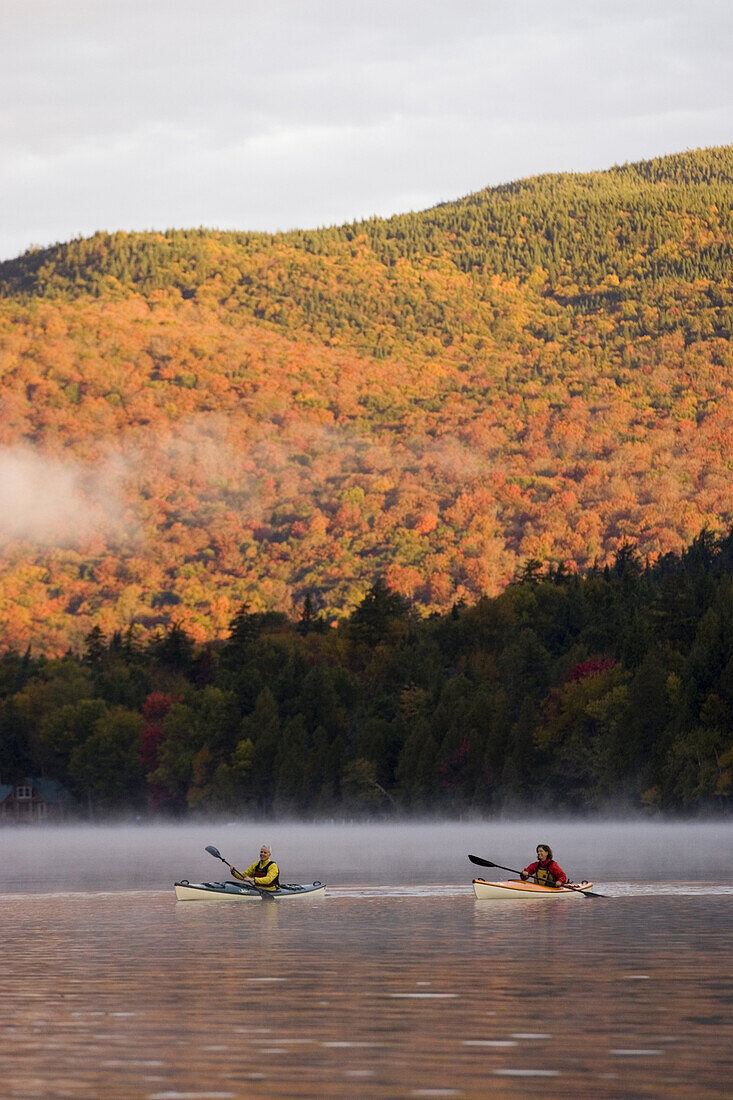 Fit, middle-age couple sea-kayak on Lake Placid in autumn, New York, USA. Photo by Henry Georgi/Aurora