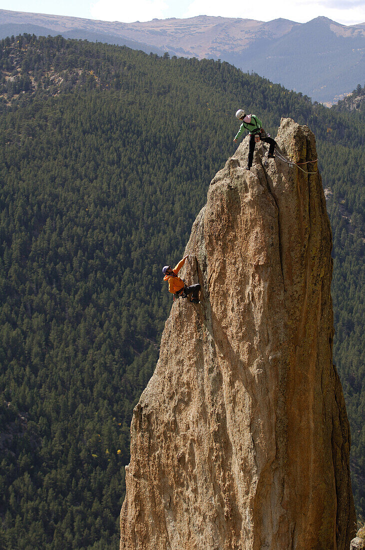 A guide on top of a rock spire gives advice to a climber during a precarious moment.  Topher Donahue / Aurora 