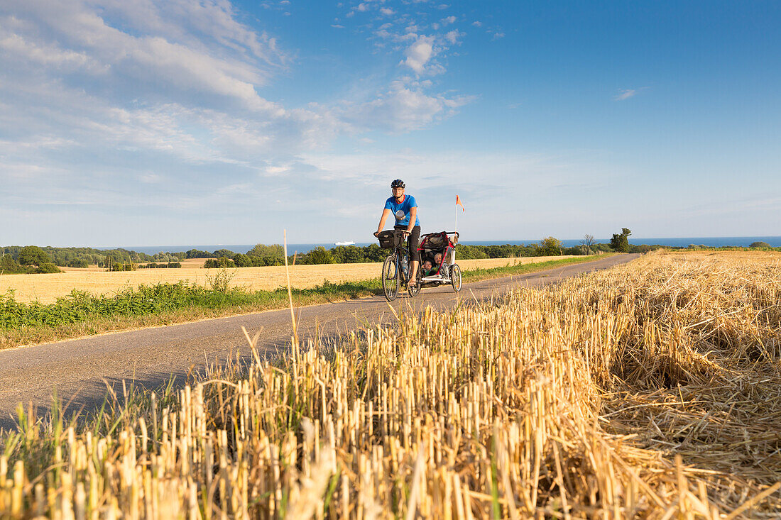 Fahrradfahrer mit Kinderanhänger auf einer Landstraße zwischen Stoppelfeldern, Klintholm, Insel Mön, Dänemark