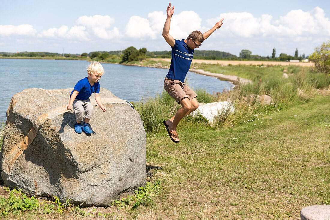 Father and son (4 years) jumping from a stone, Klodskov, Falster, Denmark