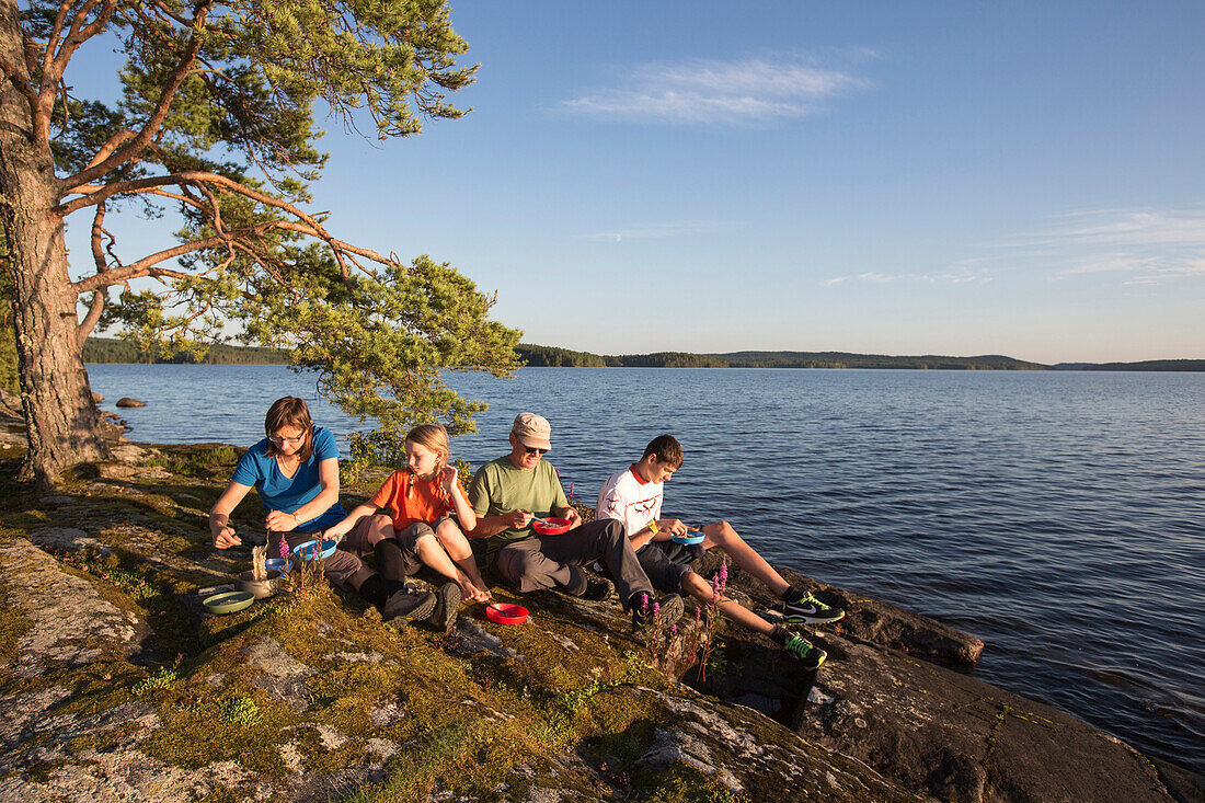 Familie beim Abendessen auf einem Felsen am Värmelnsee, Värmland, Schweden
