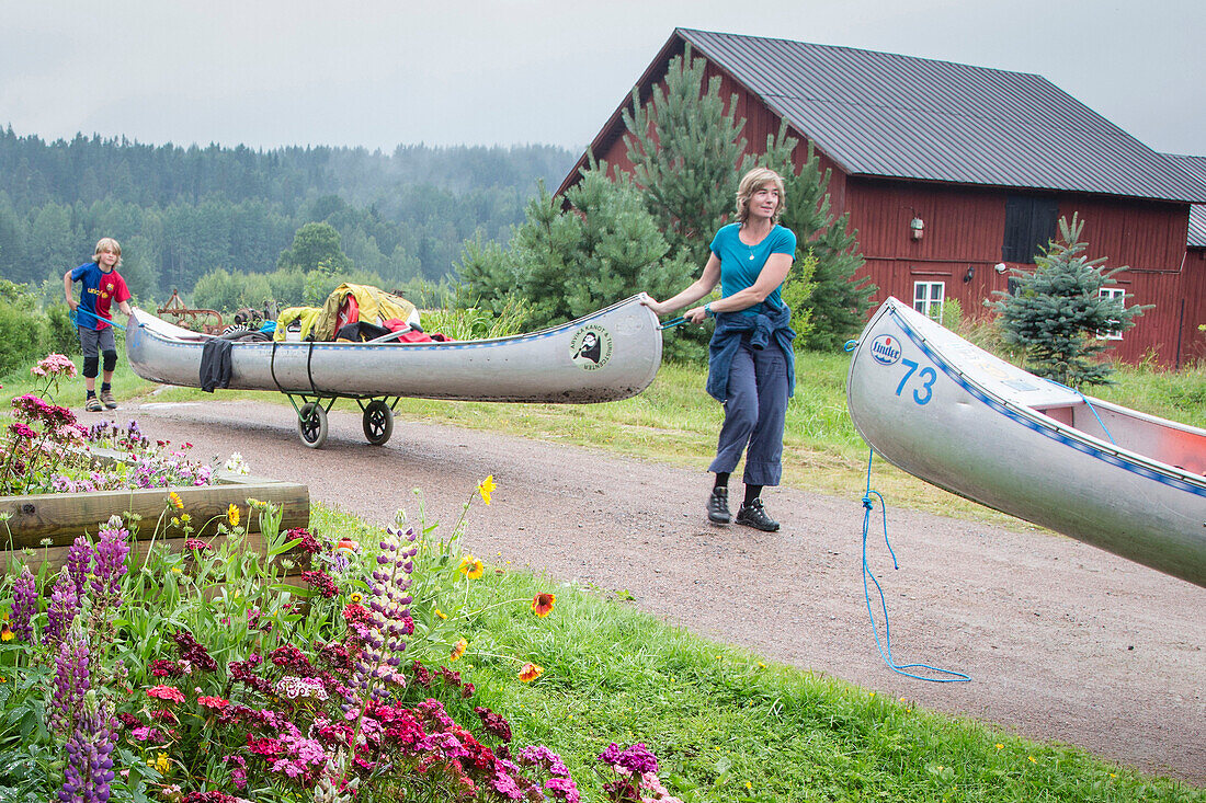 Eine Frau und ein Junge transportieren ein Kanu auf einem Weg zum Glafsfjorden See, Värmeln, Värmland, Schweden