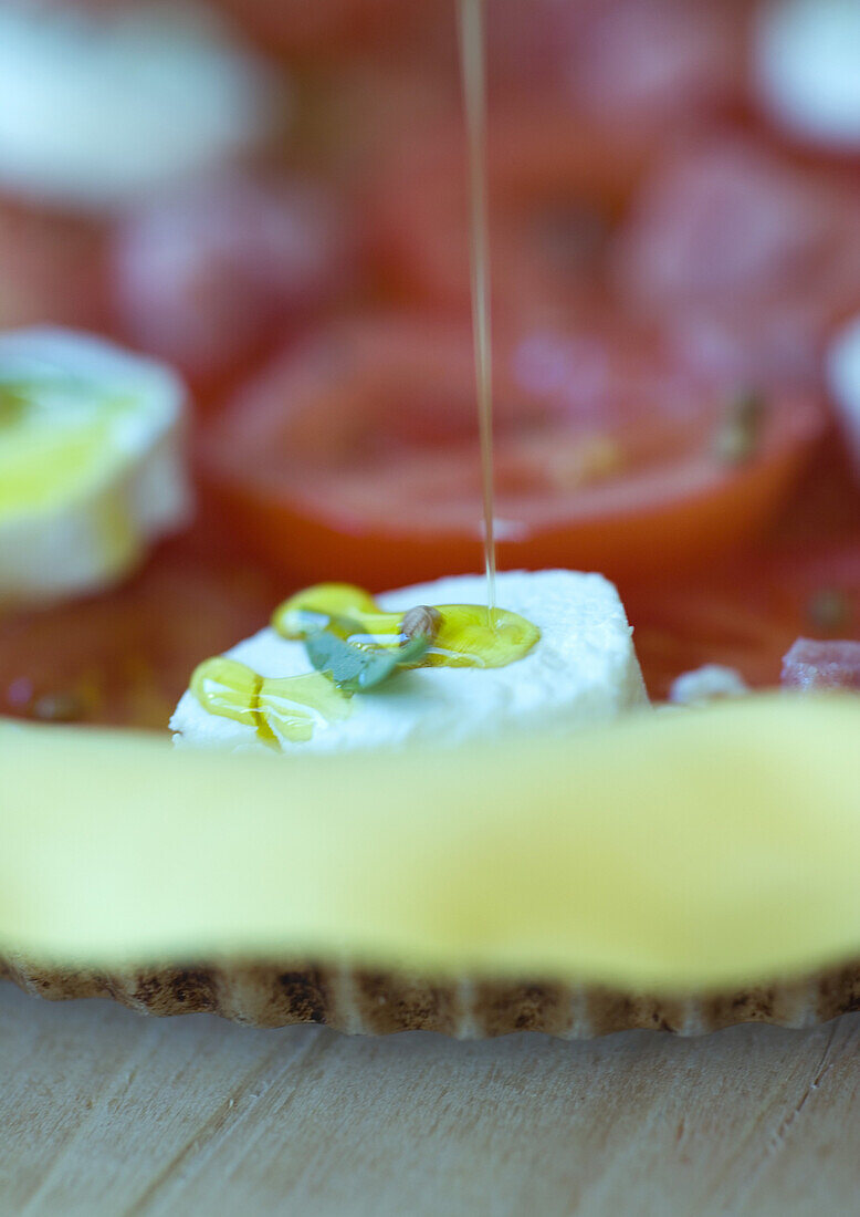 Olive oil being drizzled on uncooked tomato, goat cheese and ham tart