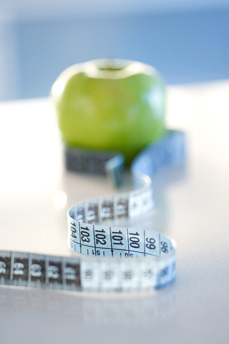 Measuring tape wrapped around green apple, close-up