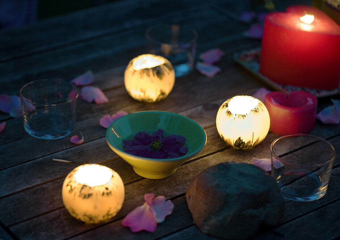 Candles glowing on table decorated with rose petals, and bowl holding floating flower