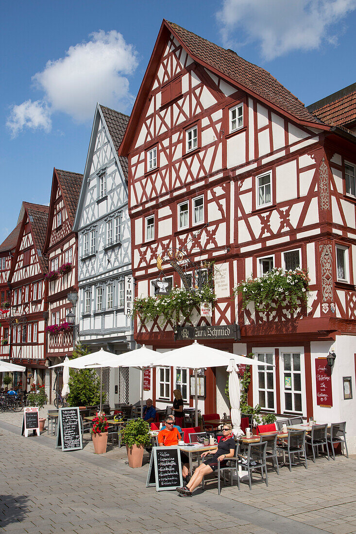 People sitting outside Gasthaus Zum Schmied restaurant near half-timbered houses in the old town, Ochsenfurt, Franconia, Bavaria, Germany