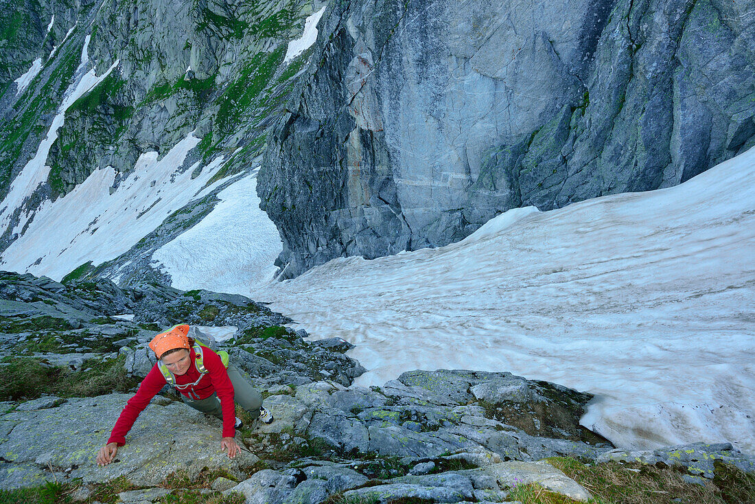 Frau klettert durch Schrofen, Schneerinne im Hintergrund, Sentiero Roma, Bergell, Lombardei, Italien