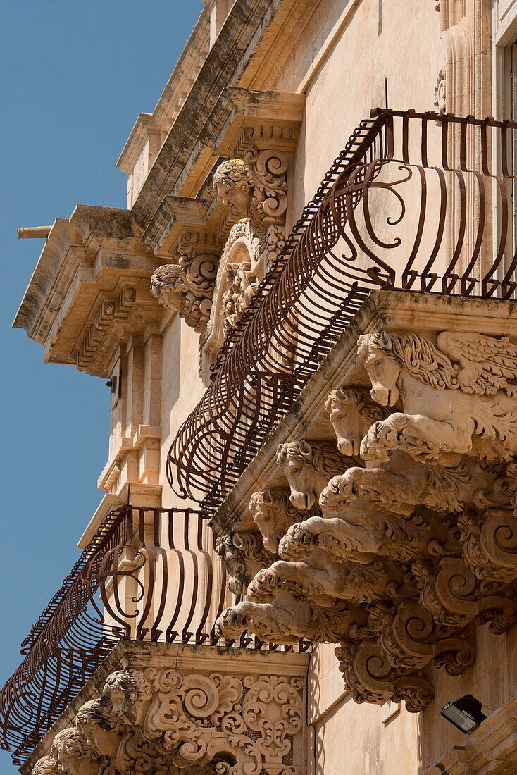 Baroque stone carvings of heads under a balcony at the Palazzo Nicolaci di Villadorata in Noto, UNESCO World Heritage Site, Syracuse Province, Sicily, Italy, Europe
