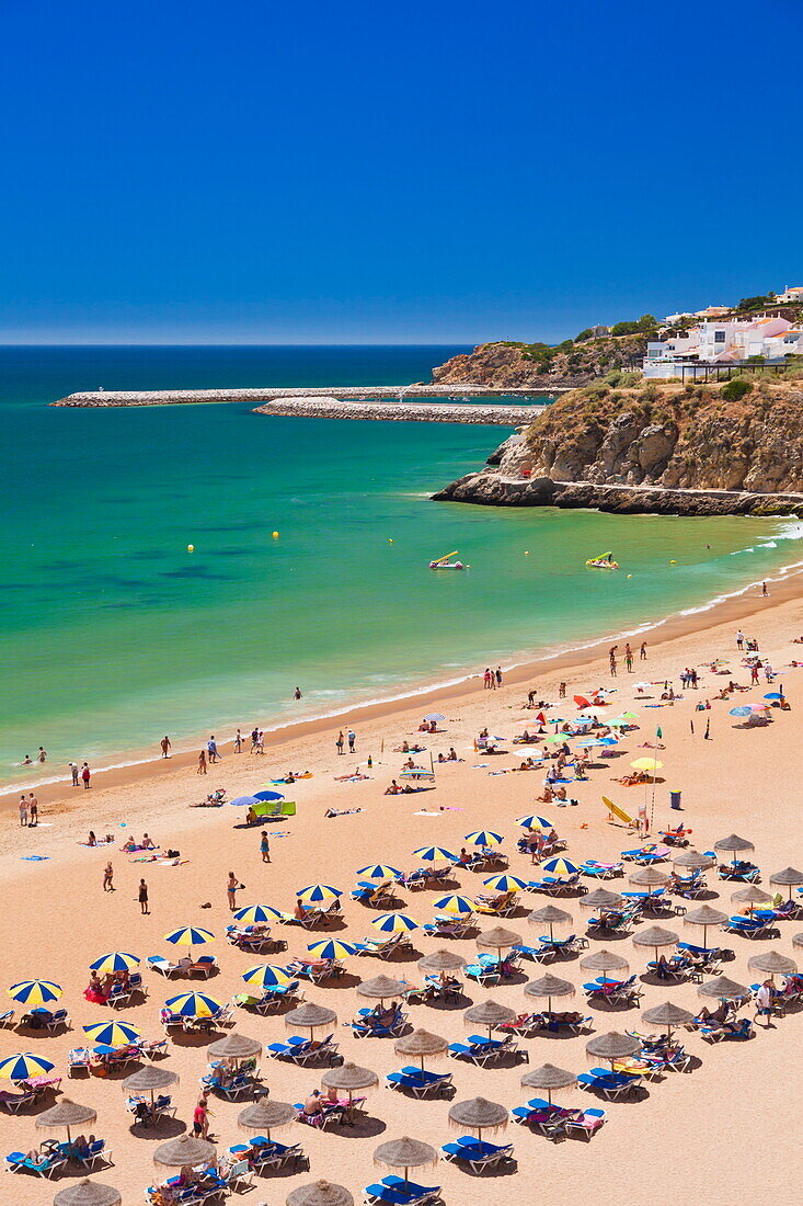 Holidaymakers sunbathing under beach umbrellas on the sandy beach at Praia do Tunel, Albufeira Beach, Algarve, Portugal, Europe