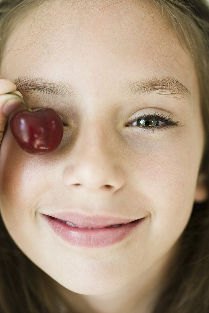 Girl covering eye with cherry, close-up