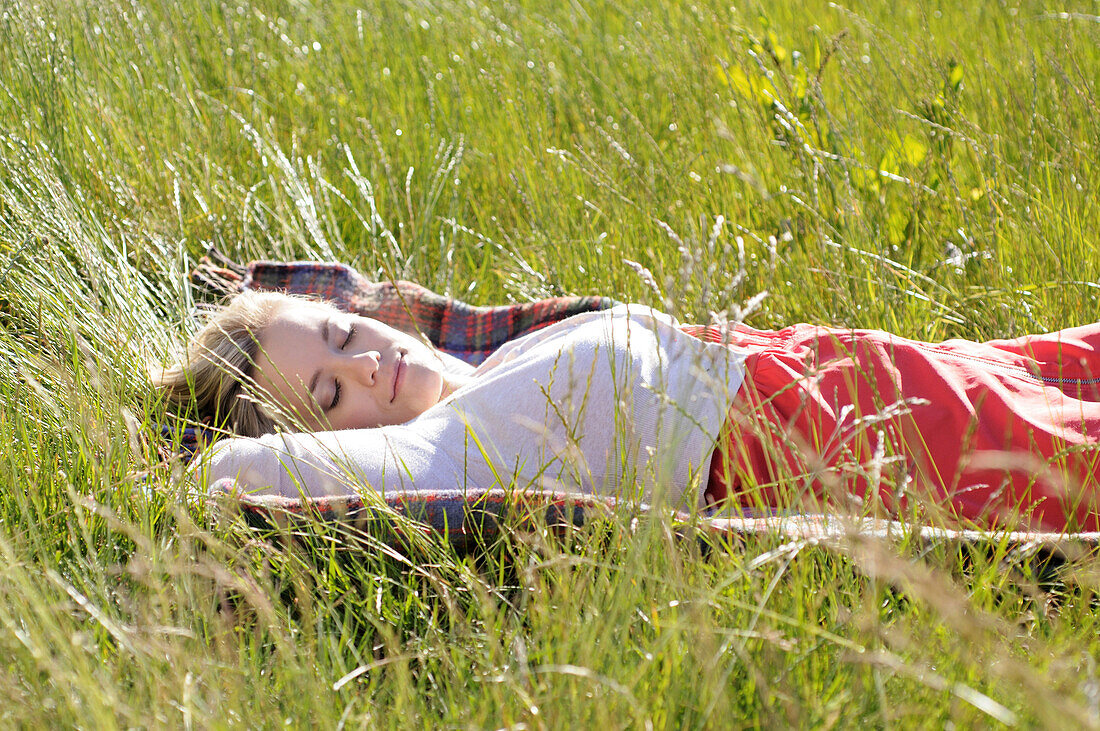 Young woman napping on blanket in tall grass