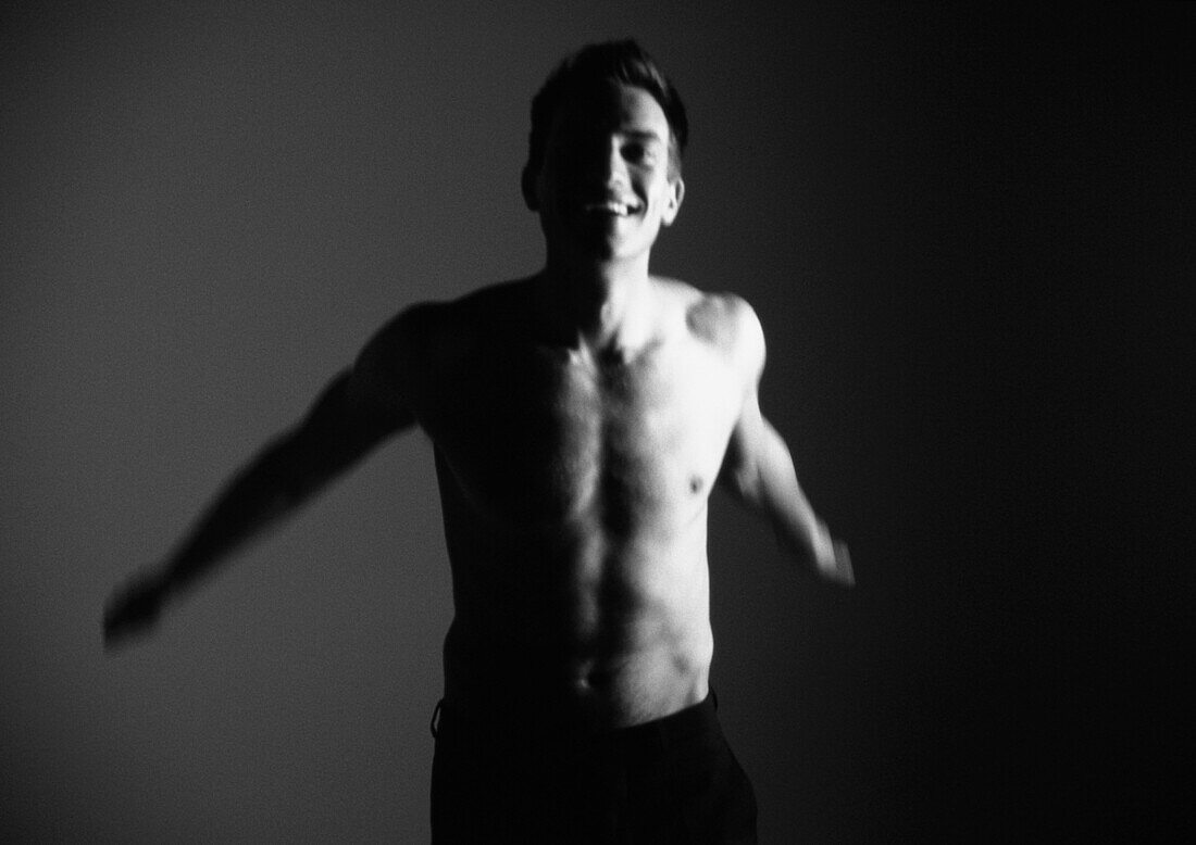 Barechested man reaching arms backwards and smiling, blurred, black and white.
