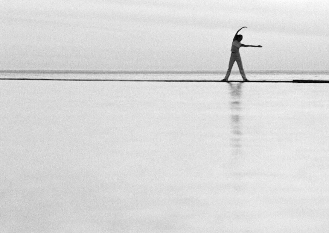 Woman exercising by the sea, b&w