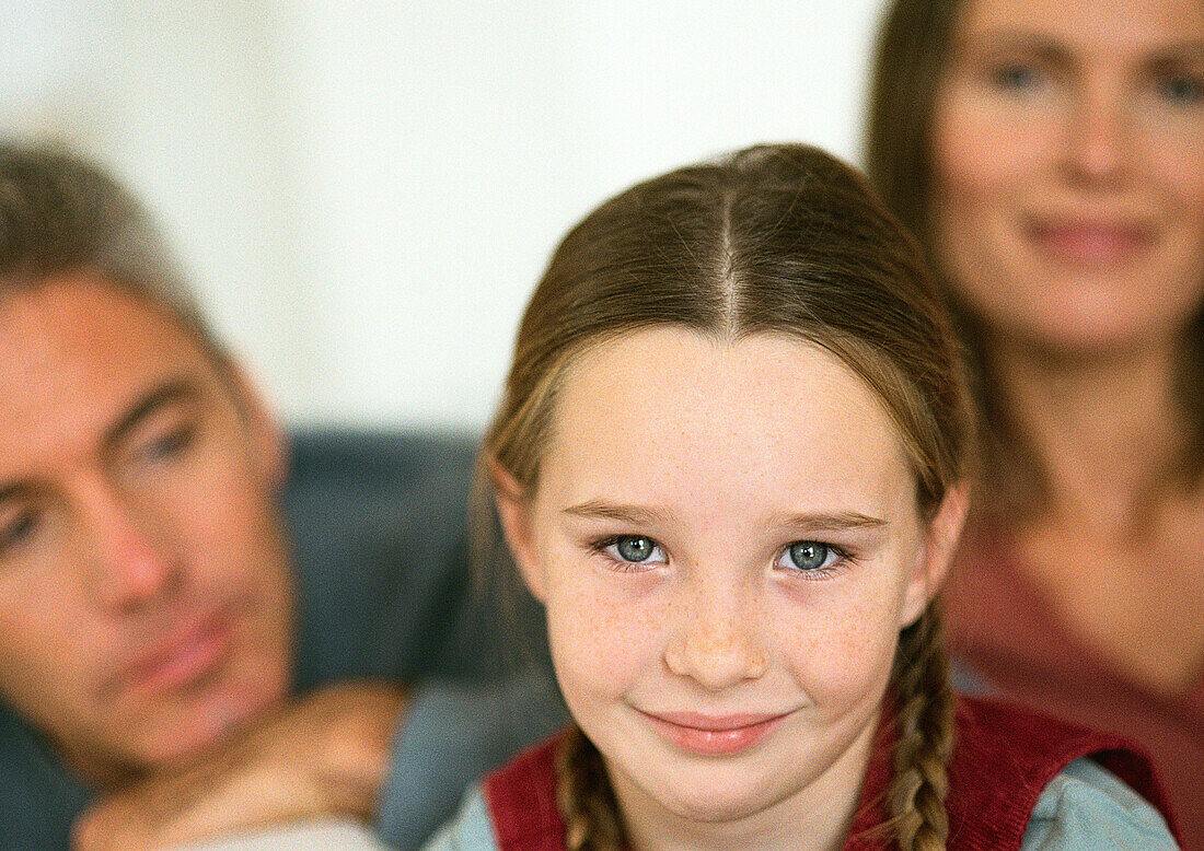 Little girl with pigtails smiling, adult man and woman in background, close-up, portrait