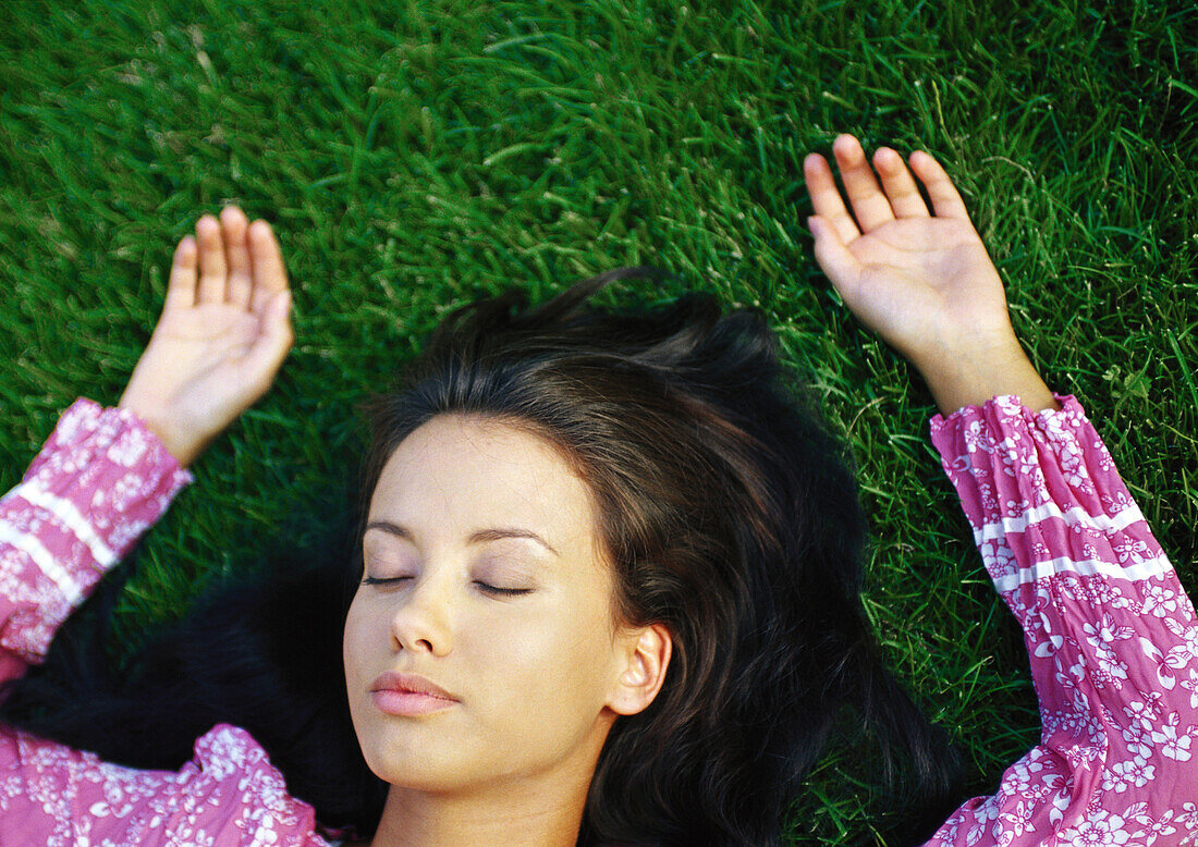 Woman lying on grass with eyes closed, close-up