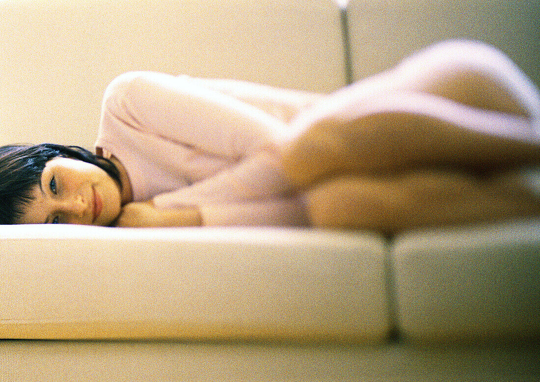 Woman lying curled up on sofa, smiling