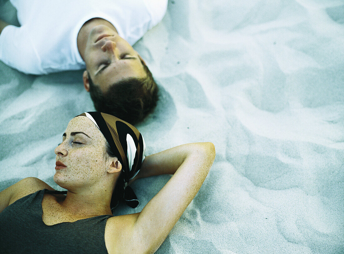 Couple lying on sand, eyes closed, elevated view