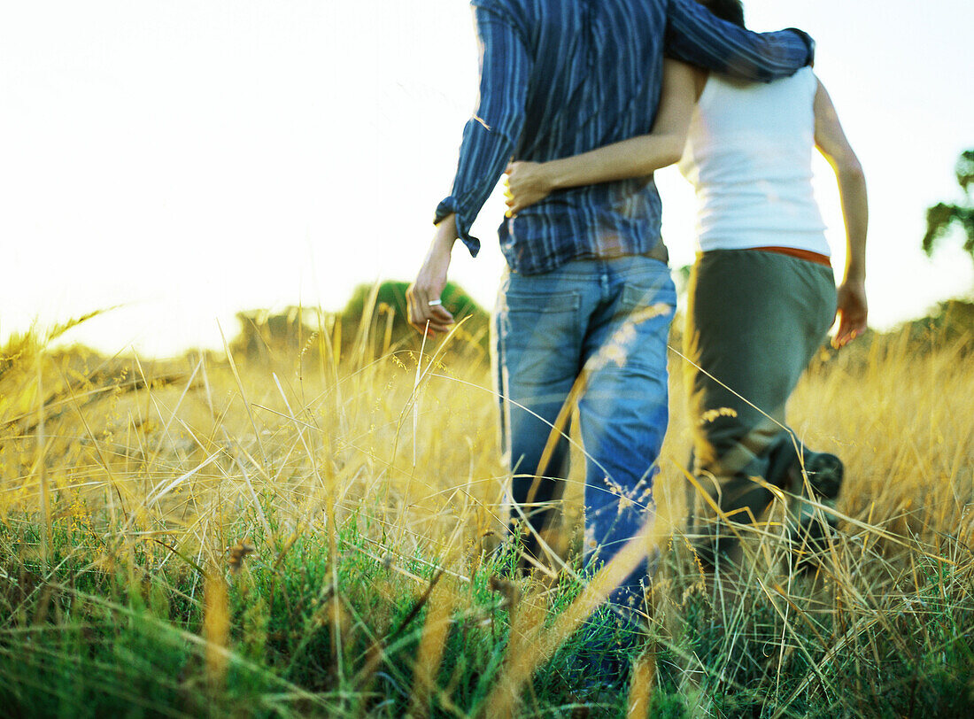 Couple walking through field, rear view, low section