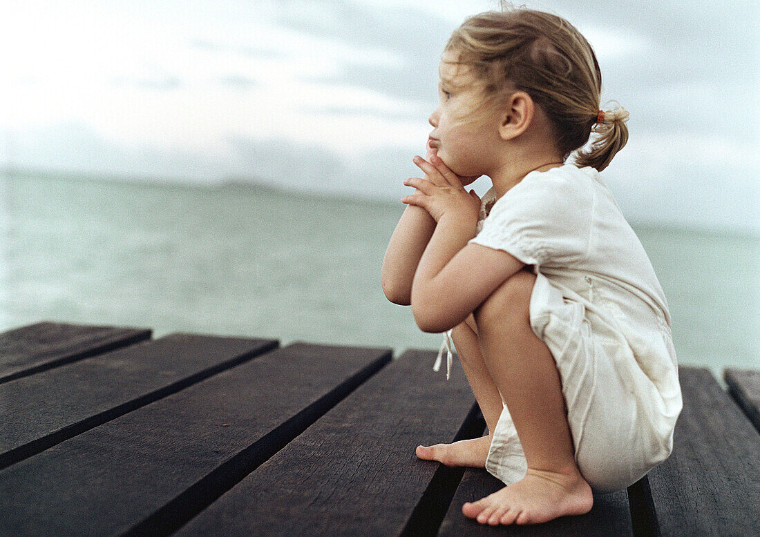 Girl crouching on dock, sea in background