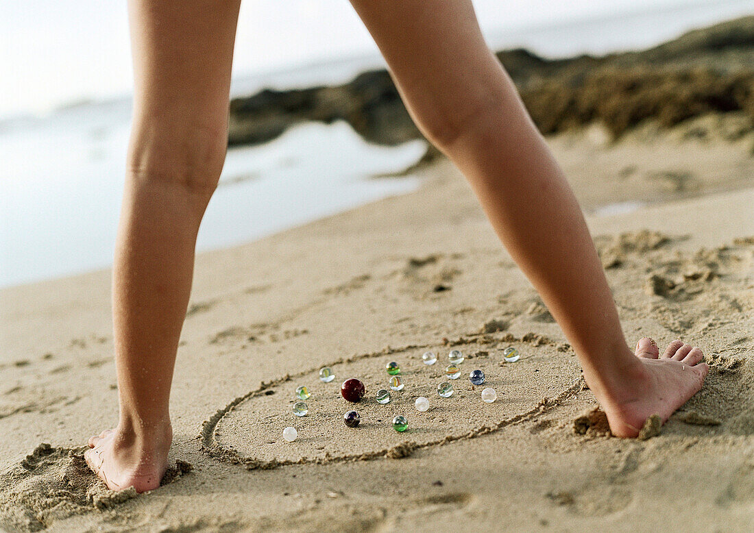 Child's legs above marbles on sand, low section, close-up