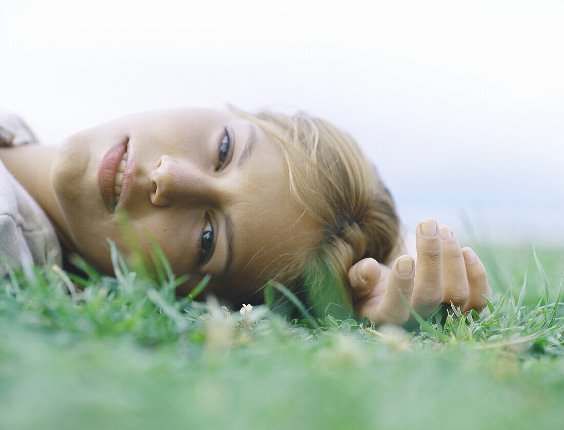 Junge Frau auf dem Rücken im Gras liegend, Hand über dem Kopf, Kopfaufnahme