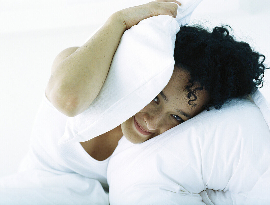 Woman in bed covering head with pillow
