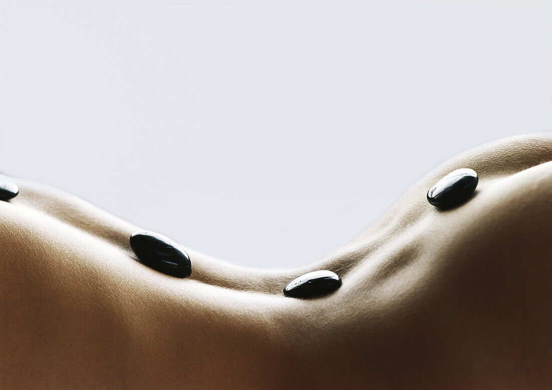 Gewölbter Rücken einer Frau mit schwarzen Steinen auf der Wirbelsäule, Nahaufnahme
