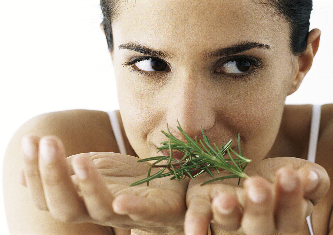 Woman holding sprigs of rosemary in palms, looking to the side, close-up