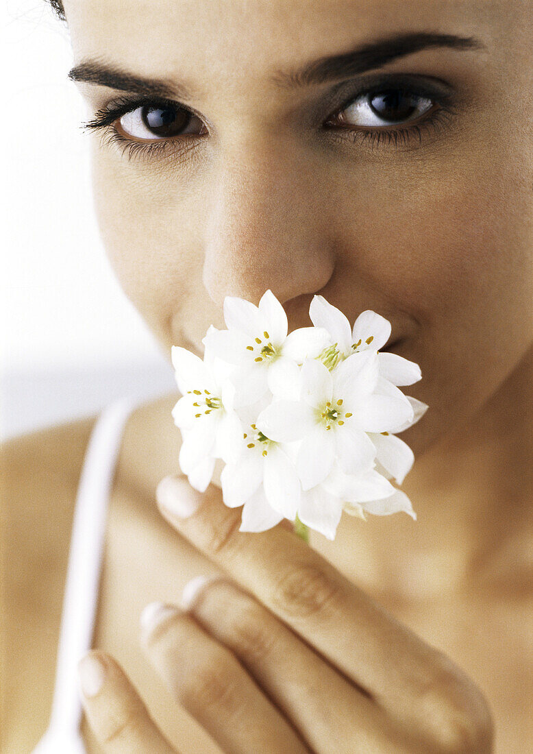 Woman holding white flowers to nose, looking at camera, close-up