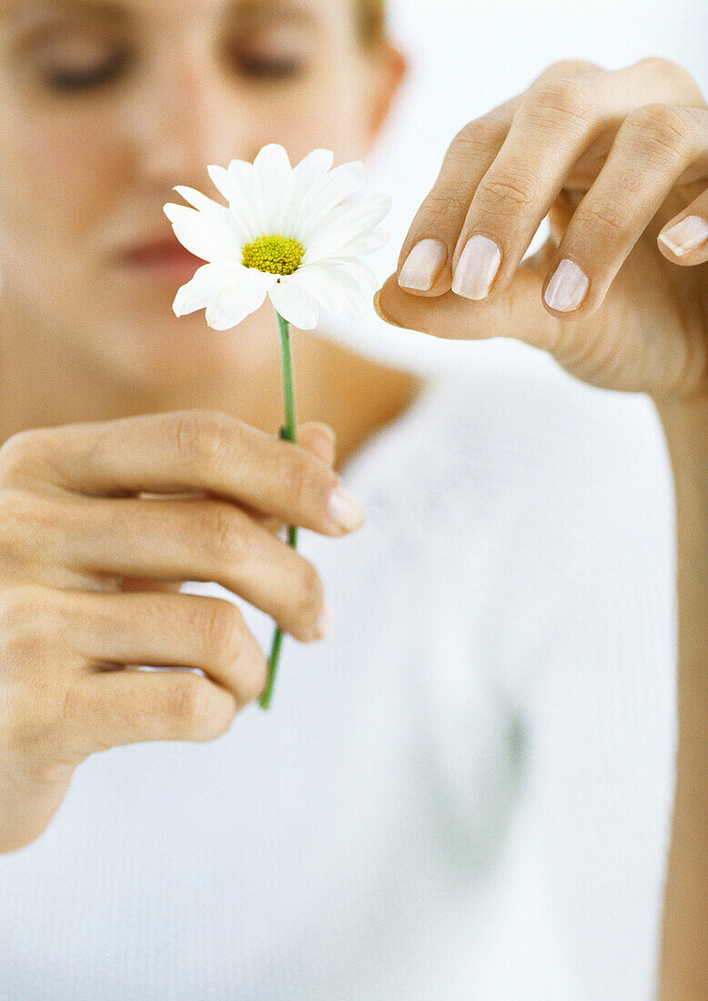 Woman plucking petals from flower with eyes closed