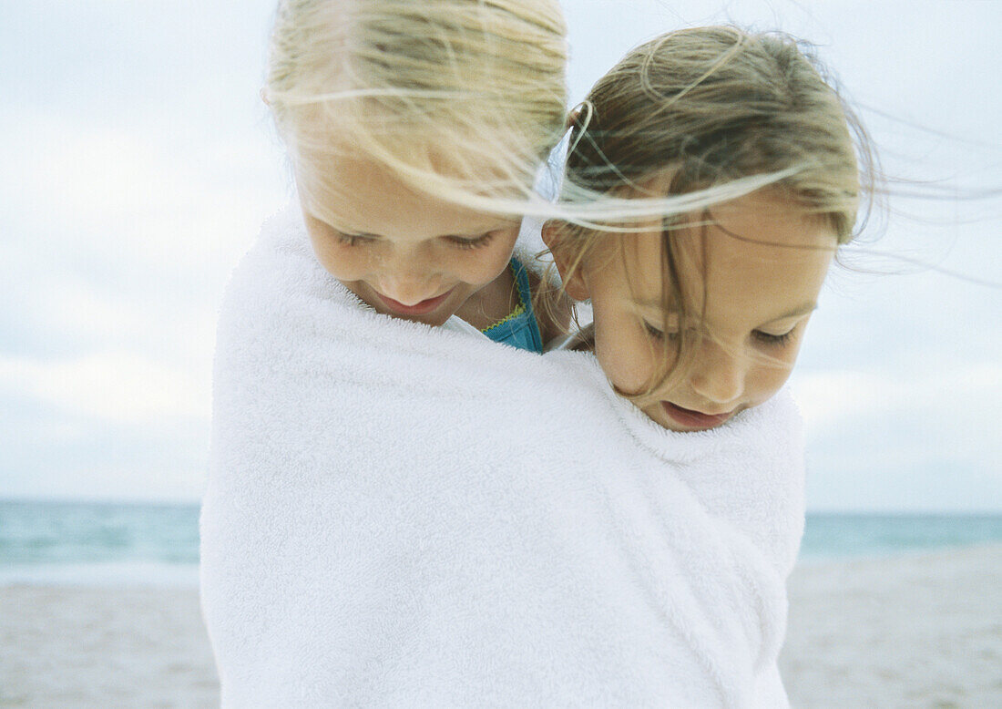 Two girls wrapped in same towel on beach