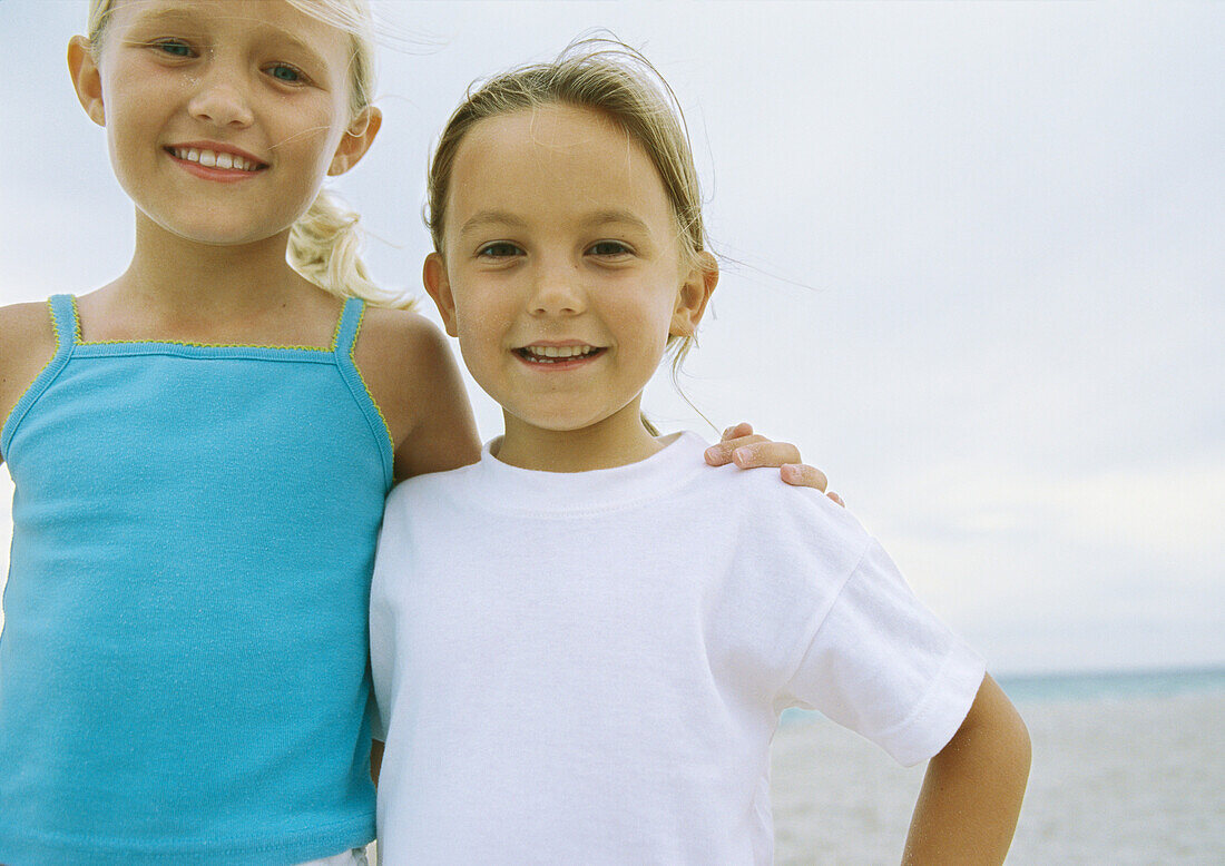 Two little girls standing side by side on beach